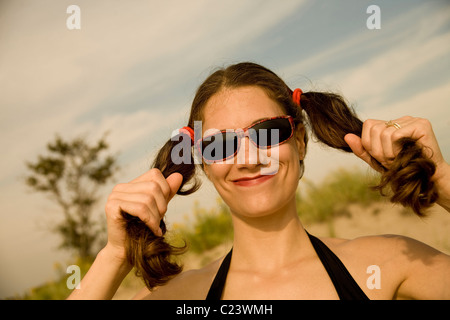 Young woman, at the beach, wearing sunglasses and holding her pigtails. Stock Photo