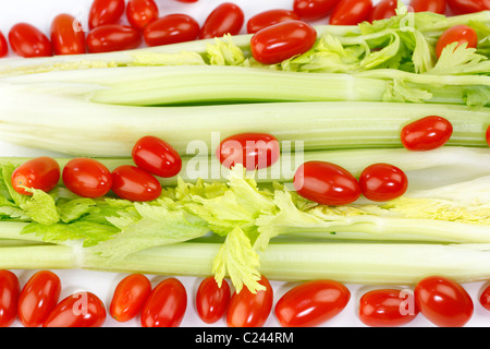 Organic celery heart stalks with small cherry plum tomatoes on a white background. Fresh long green vegetable and small round red fruit mix on white. Stock Photo