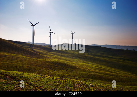 Three wind turbines silhouettes on top of hill Stock Photo