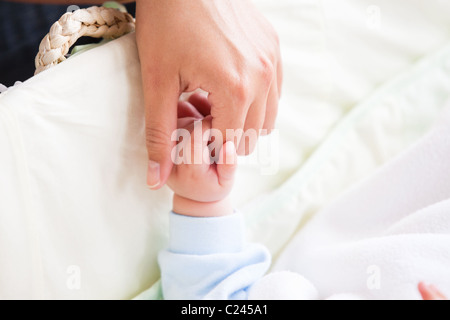 Close-up of a young mother holding the hand of her baby lying on his cradle Stock Photo