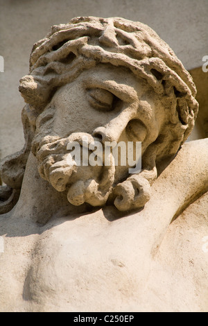 Stone statue of Christ on the cross against a blue sky at a cemetery in ...