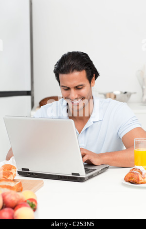 Cheerful man working on his laptop during snack time Stock Photo