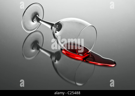 Wine glass with red wine tumbled over and wine spilled out on reflecting surface Stock Photo