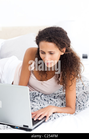 Pretty woman working on her laptop lying on her bed Stock Photo