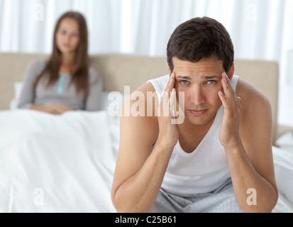 Tired man having a headache sitting on the bed with his girlfriend Stock Photo