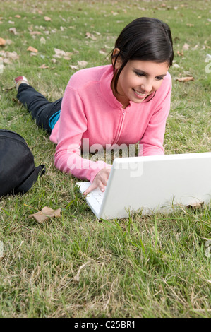 woman, lay, laying, down, on, a, the, field, campus, field, outdoors, park, exteriors, with, mac, laptop, netbook, notebook. Stock Photo