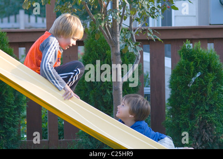 Brothers stopping for conversation on backyard slide age 8 and 5. St Paul Minnesota MN USA Stock Photo