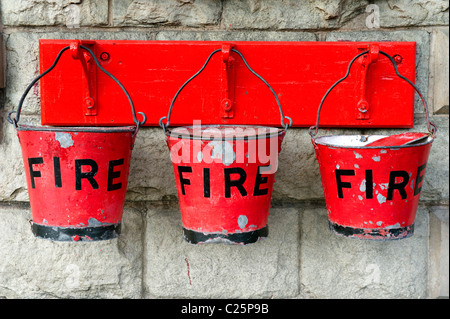 Row of three old red fire buckets hanging from a wall Stock Photo