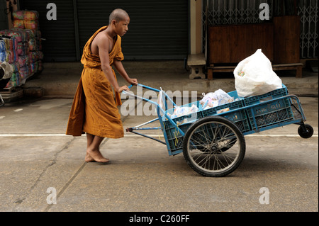 young novice monk pushing cart with food collecting on morning alms round , mae sot, northern thailand Stock Photo