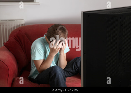 Young male watching TV sport at home head in hands. Stock Photo