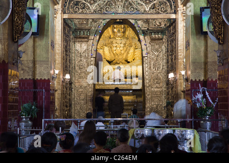 Praying people, Gold Buddha statue thick covered by gold leafs from prayers donations. Maha Mayat Muni temple, Mandalay, Burma. Stock Photo