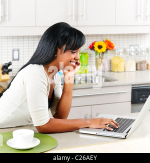 Smiling black woman using computer in modern kitchen interior Stock Photo