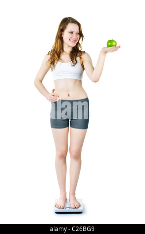 Healthy happy young woman holding green apple standing on bathroom scale Stock Photo