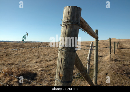 A fencepost and fence line with an oil pump jack in the background. Stock Photo