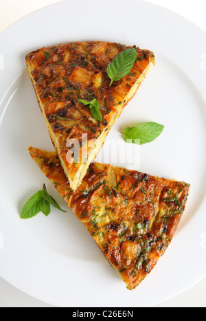 Slices of Spanish omelet or tortilla de patatas on a white plate, garnished with mint leaves Stock Photo