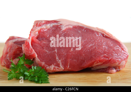 Two veal sirloin steaks on a wooden chopping board with a white background and a sprig of parsley Stock Photo