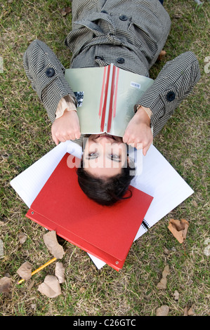 Lady, woman, body, lay, laying, down, hold, holding, a, book, red, on, a, field, campus, outdoor, outdoors, exterior, outside,. Stock Photo
