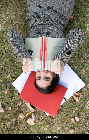 Lady, woman, body, lay, laying, down, hold, holding, a, book, red, on, a, field, campus, outdoor, outdoors, exterior, outside,. Stock Photo