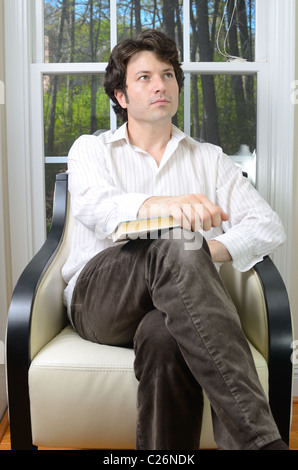 Young adult male looking off into the distance with a book on his lap. Stock Photo