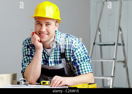Portrait of a cheerful repairman in helmet sitting at table Stock Photo