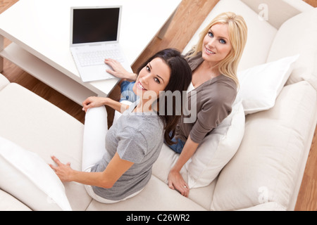 Overhead photograph of two beautiful young women at home sitting on sofa or settee using a laptop computer and smiling Stock Photo