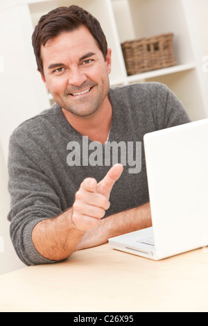 Smiling man in his thirties at home using his laptop computer and pointing to camera Stock Photo