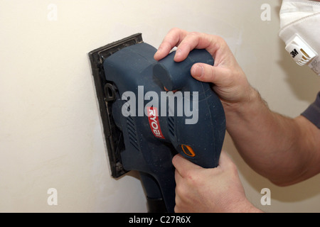 DIY sanding a wall smooth with an electric power tool Stock Photo