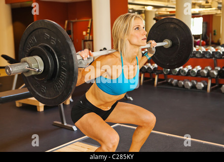 A physically fit woman doing squats in a health club weight room. Stock Photo