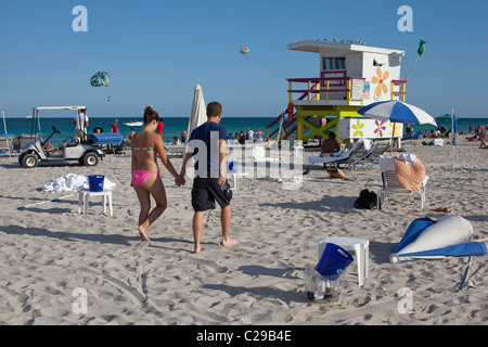 A couple walk holding hands in front of  one of the original decorated lifeguard huts of Miami beaches, Florida, USA Stock Photo