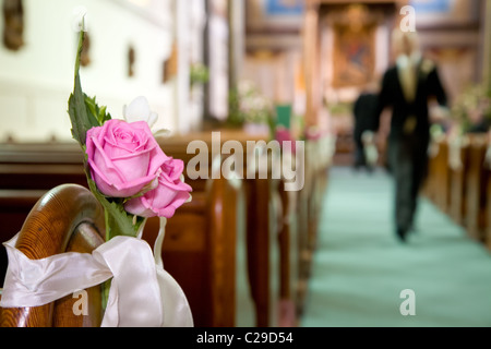 Pink roses tied to a church bench with an usher walking down the isle Stock Photo