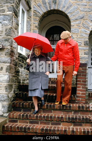 Elderly couple working their way carefully down brick steps in the rain Stock Photo