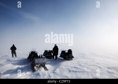 A blowing snow landscape with three snowmobiles on an expedition Stock Photo