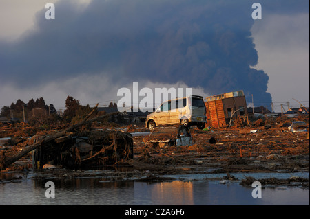 Swept cars on the debris after the great earthquake and tsunami hit the north east coast of Japan.  The smoke in the background Stock Photo