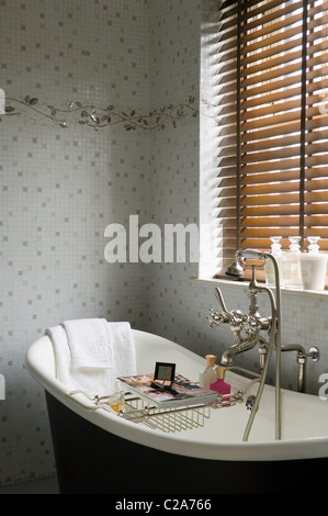 Freestanding bath under closed blinds with wall motif tiling Stock Photo