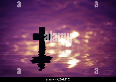 Silhouette of a Cross above the water with reflection  in the sunset time on a sunny cloudy summer evening. Space for text. Stock Photo