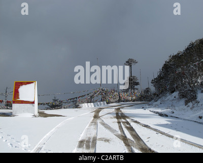 Roas in the snow, sign and prayer flags at Thrumshingla Pass, the border between central and eastern Bhutan Stock Photo