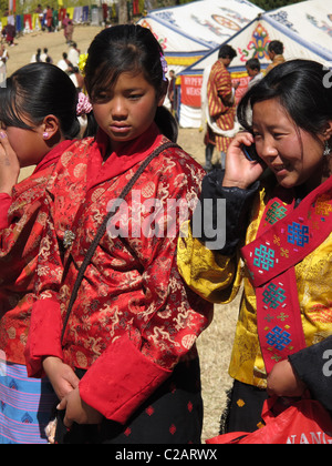 Young Bhutanese people, one with a mobile phone, traditionally dressed during the Paro Festival, Bhutan Stock Photo
