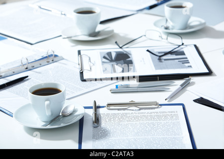 Close-up of eyeglasses, documents, pens, cups of coffee on the table