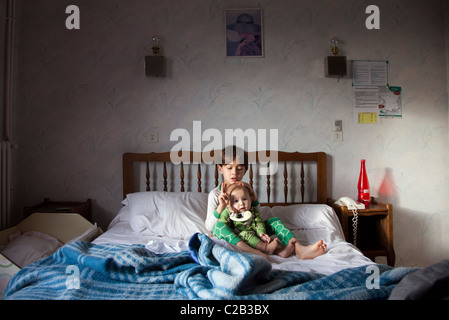 Little boy sitting with his baby sister on hotel bed Stock Photo