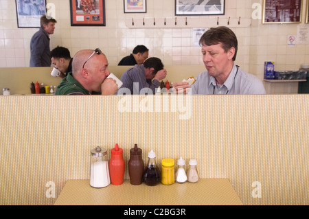 Condiment bottles Sugar, Ketchup, Brown Sauce, Vinegar, Mustard, Salt, Pepper on table. Man eating a sandwich and drinking a cup of tea. Cafe sauce bottles. Regency Cafe Westminster London SW1 UK. 2010s HOMER SYKES Stock Photo