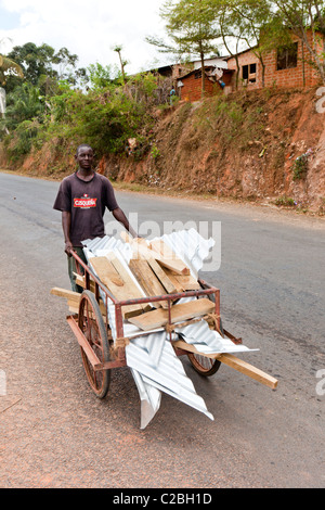 African man transporting corrugated iron roofing sheets on wooden hand cart, Kisarwe Village, near Dar es Salaam, Tanzania Stock Photo