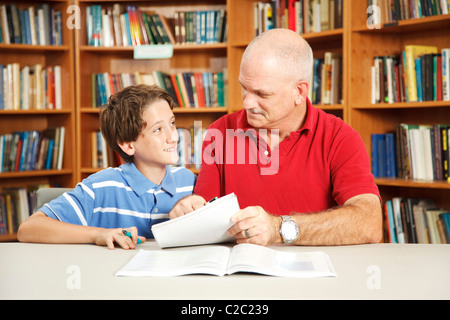 Father or male teacher tutoring a young student in the school library.  Stock Photo