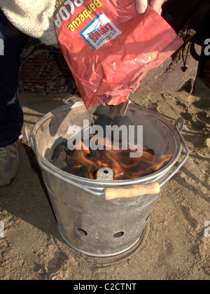 Feeding Charcoal into a lit barbecue on the beach Stock Photo