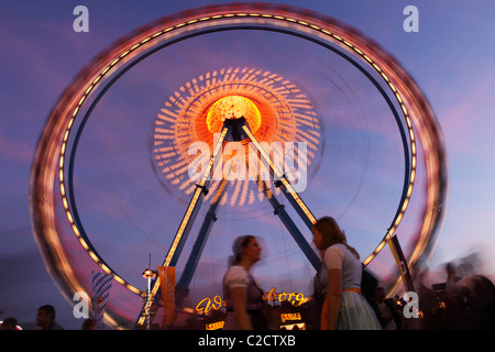 People meet at dusk under the big wheel at the Oktoberfest funfair, held every autumn on the Theresienwiesen in Munich. Stock Photo