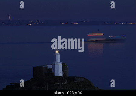 ship leaves on the high tide at night from the safety of a calm bay. Lighthouse marks the point of first and last contact.  Mumbles Lighthouse. Stock Photo