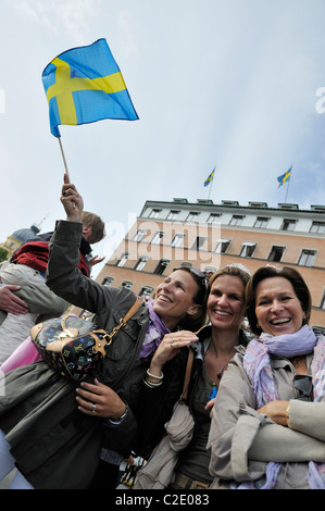 Three middle-aged women smiling and waving little Swedish flag during the Royal Wedding Festivities in Stockholm, Sweden Stock Photo