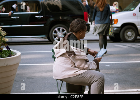 A reader uses her Amazon Kindle electronic book in a pedestrian mall on Broadway in New York Stock Photo