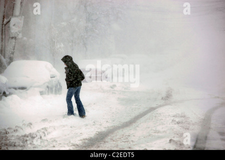 A woman crosses a snow covered street during a winter storm in Boston Massachusetts Stock Photo