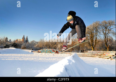 A man rides a snowboard on a snow covered skatepark in Kelvingrove Park, Glasgow, Scotland. Stock Photo