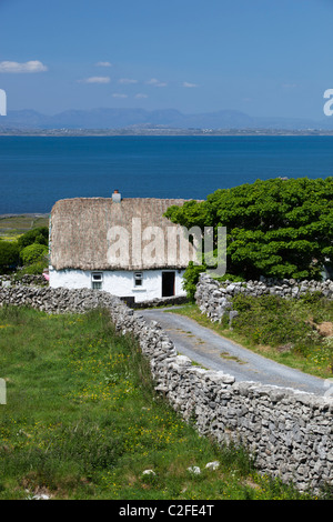 White-washed thatched cottage with dry stone walls and Galway Bay behind Stock Photo